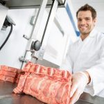 Homem cortando carne com equipamento especial no açougue