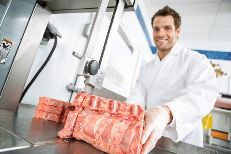 Homem cortando carne com equipamento especial no açougue